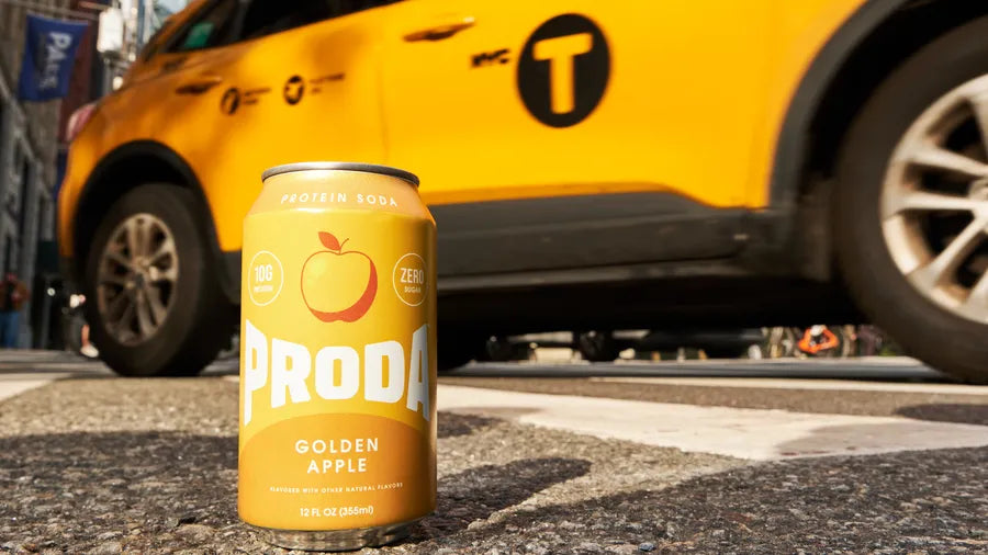 A can of PRODA Golden Apple on the street beside a yellow New York taxi.