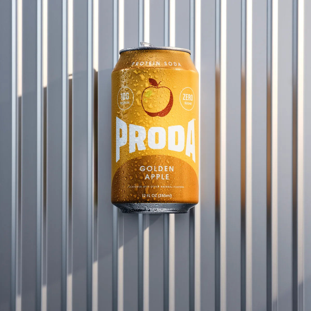 A can of PRODA Golden Apple against a ribbed silver suitcase