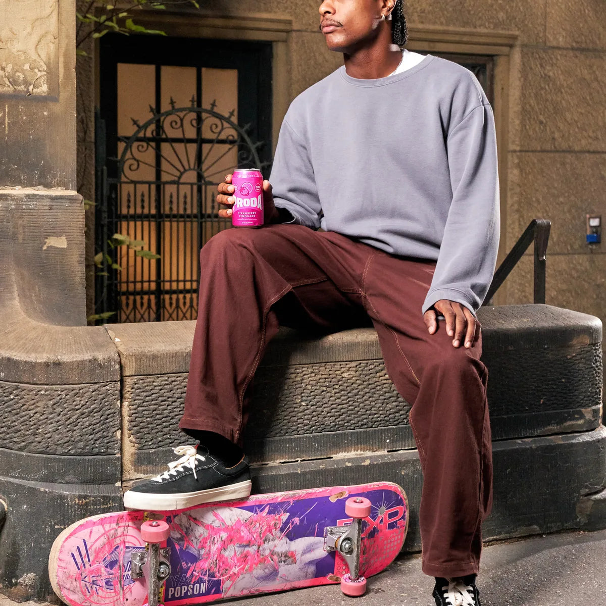 A man on a brownstone stoop with a skateboard and a can of PRODA Strawberry Lemonade